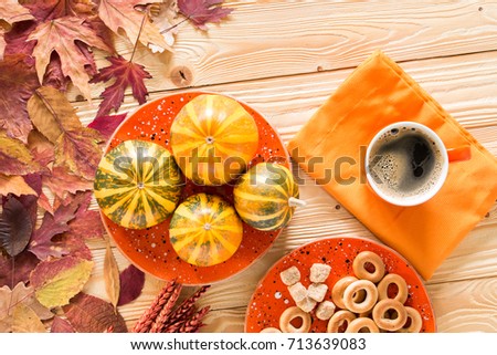 cup of coffee, decorative pumpkins, bagels and cane sugar on wooden table decorated by falling leaves, top view