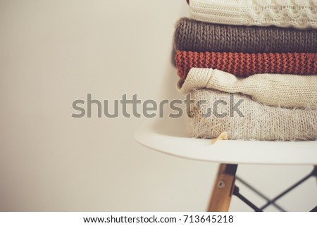 a stack of knitted warm cozy clothes, on a chair by the white wall. autumn concept.
