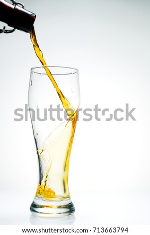 Beer is pouring from a bottle into an empty glass, white background, studio light