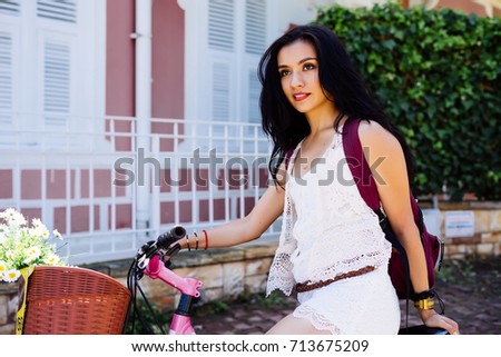 Young beautiful black-haired girl riding a bike around the city on a sunny day