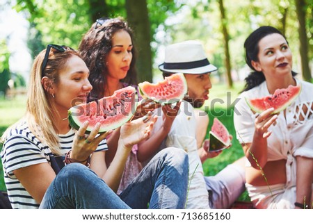 Group of friends having pic-nic in a park on a sunny day - People hanging out, having fun while grilling and relaxing.