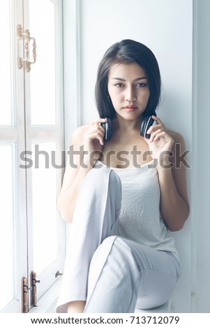 Beautiful girl sitting and relax with listening to music at the window happily.