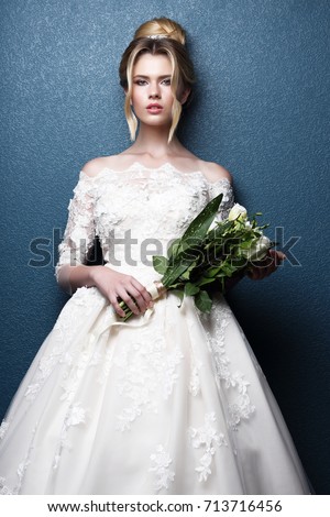 Young beautiful bride. Wedding hairstyle, blond hair, wedding dress, makeup and bride's bouquet. Indoor shot