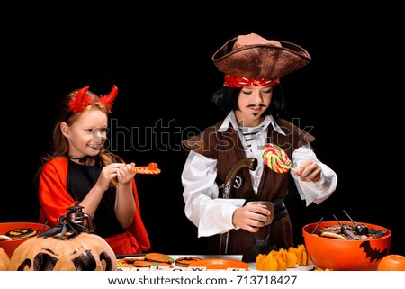 children in halloween costumes of devil and pirate with halloween sweets, isolated on black  