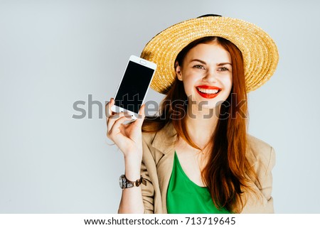 A young girl in a hat smiles, holds a phone in her hand. Isolated on a gray background