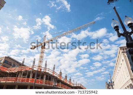 Working crane and safety net on modern office and residential building under construction near other skyline against cloud blue sky in Downtown New Orleans, Louisiana, US. Red grid prevent object fall