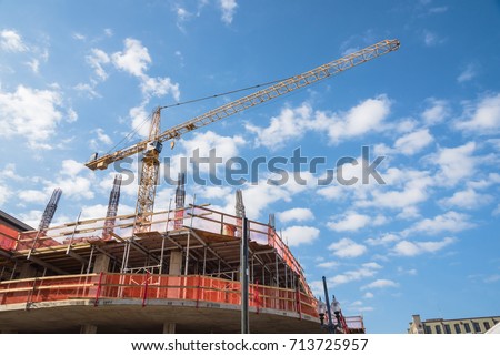 Working crane and safety net on modern office and residential building under construction against cloud blue sky in Downtown New Orleans, Louisiana, US. Red grid prevent objects falling from height.