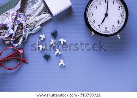 Overhead of school/office supplies and alarm clock on blue background.  Subject capture against soft window lighting. Copy space.