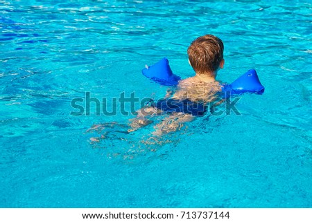 The boy learns to swim in the pool with auxiliary inflatable belts. Blue pool water
                                Royalty-Free Stock Photo #713737144