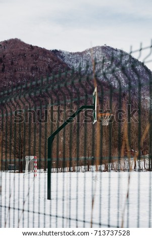 Metal fence with blurred basketball court in winter. 