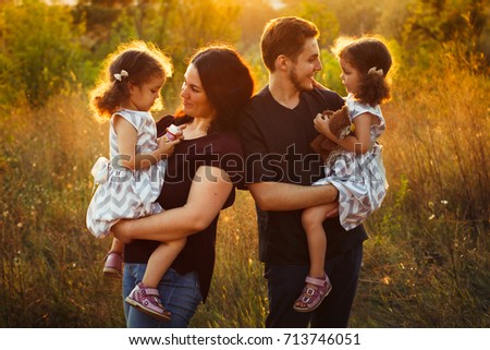 Family portrait of four in autumn forest park with little girls twins. Happy people, smiling and kissing. Warm evening sunlight