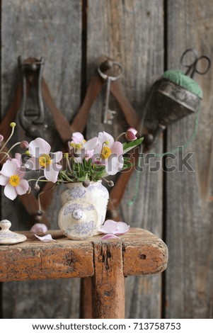 Flowers in small vintage jar on aged authentic wooden stool on coat rack background, real vertical photo