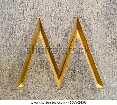 Yellow or Gold Alphabet 'M' on Cement Background 