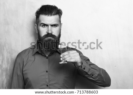 Bearded man, long beard. Brutal caucasian serious hipster with moustache in brown shirt holding alcoholic red shot on golden texture background