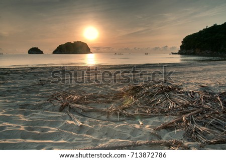 Dramatic scene to Ko Rawing from the beach under in the morning with mess up coconut leaf lay on the sand with sunrise and island in the background, Ko Rawing south of Thailand view