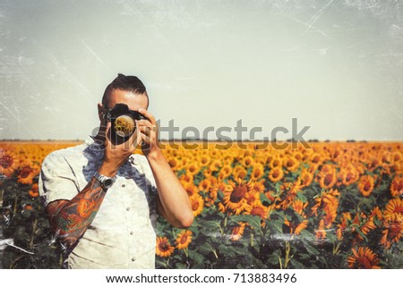 Portrait Of Male Photographer Making Photo With Camera In Hands Outdoors On Sunflowers Field With Toned Filter