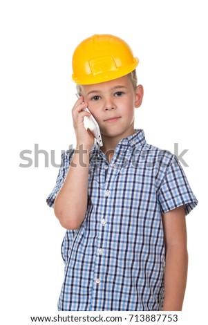 The boy in builder's helmet and blue checkered shirt speaks by phone, isolated on white background