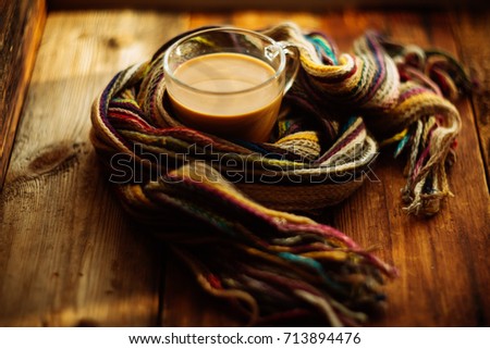 mug is wrapped by a striped knitted scarf, concept background on the topic of coziness, comfort, warmth