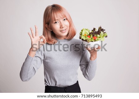 Healthy Asian woman show OK with salad on gray background