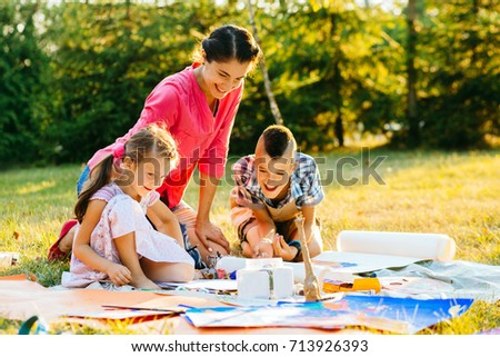 Happy mother and two kids are painting in the park. The concept of a happy family.