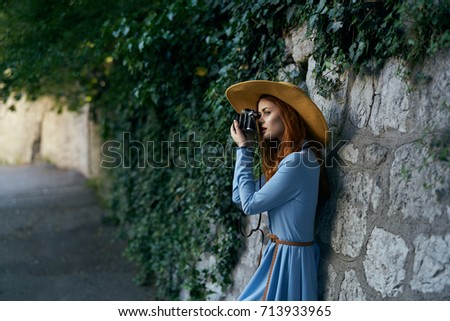 woman in a hat and in a blue dress takes pictures on the camera on the street.