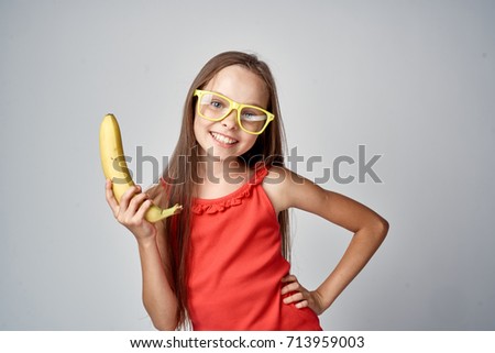 a girl in yellow glasses with long straight hair holds a banana.