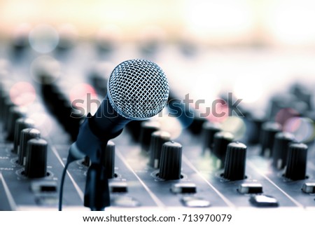 Close up microphone on blur audio mixer knops (digital audio mixing studio equipment) in recording studio with bokeh light background.