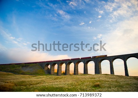 Train crosses the famous Ribblehead Viaduct. The Ribblehead Viaduct or Batty Moss Viaduct carries the Settle–Carlisle Railway across Batty Moss in the valley of the River Ribble at Ribblehead. Royalty-Free Stock Photo #713989372