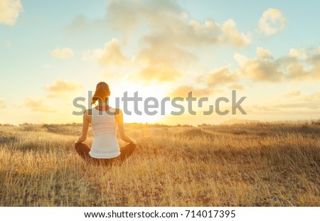 Woman meditating against a beautiful sunset. Mind body spirit.  Royalty-Free Stock Photo #714017395
