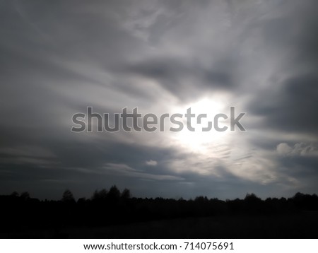 The sun among the blurry clouds in the grey sky above the horizon