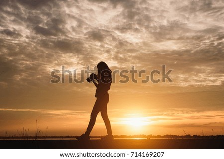 Silhouette young woman photographing landscape . Female photographer holding a camera at sunset