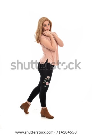 
full length portrait of girl wearing simple pink shirt and pants, standing pose on white studio background.