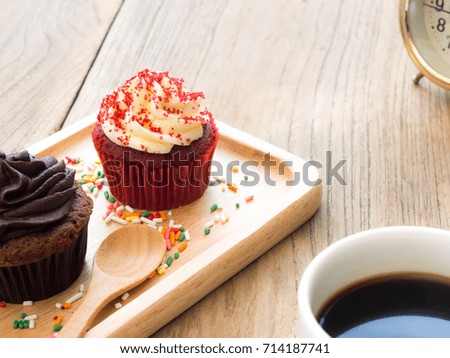 Red and chocolate cupcakes put on a spherical wooden plate. Beside of cupcake have Cactus and white coffee mug.All of it rests on wooden table.