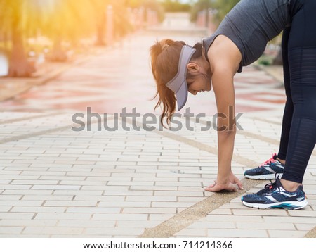 Woman athlete, Asian woman runner stretching her legs and lower body after exercise and working out with beautiful sunset background in a park