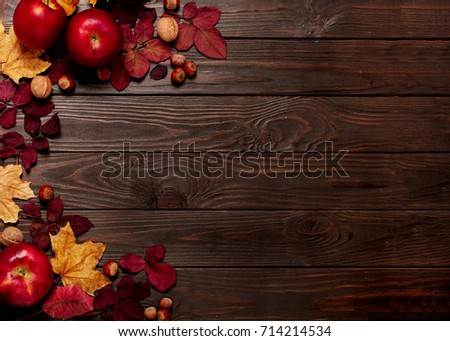 Flat lay frame of autumn crimson and yellow leaves, hazelnuts, walnuts and apples on a dark wooden background. Selective focus.