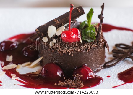 Chocolate cake on white plate with decoration from cherry, almond and mint. Delicious dessert serving in restaurant, close up picture