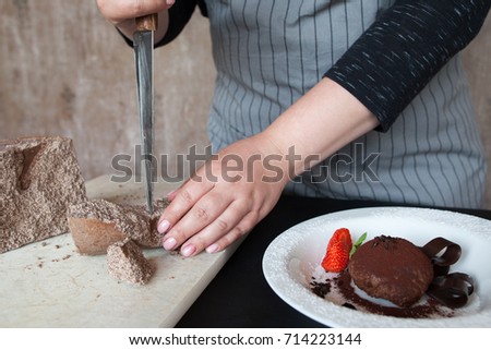 Cook woman breaks off piece of chocolate for decoration of delicious fondant in restaurant. Process of making culinary art, close up picture