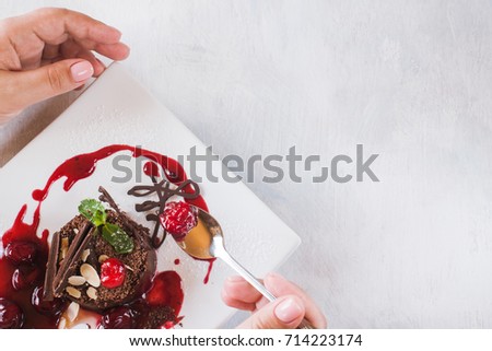 Tasting of chocolate cake with cherry jam, decorated by sweet red berry, almond and mint. Delicious dessert serving in restaurant, close up picture with free space on white background
