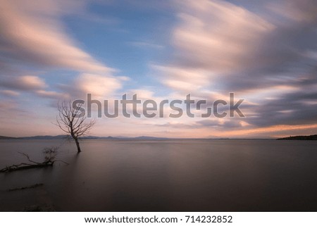 Surreal long exposure view of a lake at sunset, with tree and spectacularly moving clouds