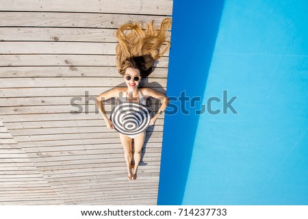 Woman lying with sunhat on the poolside near the basin with blue water. Geometric top view with copy space