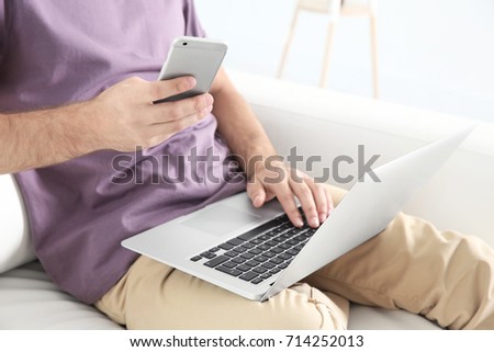 Young man searching information using laptop and phone at home