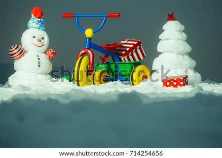 Tricycle with present box on snowy background. Snowman and snow xmas tree on grey sky. Christmas and new year celebration. Festive surprise and gifts. Winter holidays concept