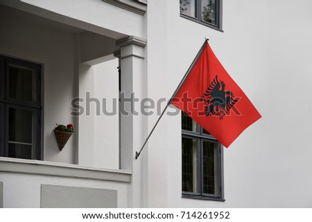 Albania flag. Albanian flag displaying on a pole in front of the house. National flag of Albania waving on a home hanging from a pole on a front door of a building.
