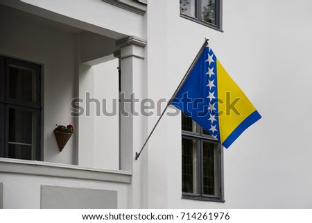 Bosnia and Herzegovina flag displaying on a pole in front of the house. National flag of Bosnia and Herzegovina waving on a home hanging from a pole on a front door of a building.