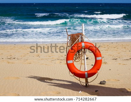 Swimming circle. Life buoy red color on beach with bright sand and sky background. Two warning signs. Safety guard, lifebuoy, lifeguard. Vacation at ocean.