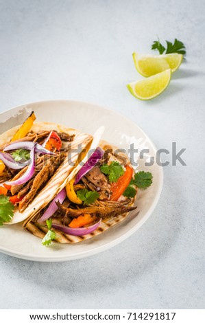 Pulled pork taco with onions and colored pepper, served with tortillas