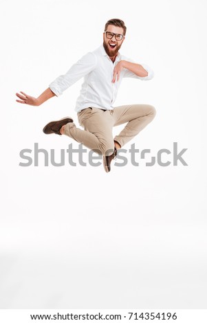 Photo of cheerful young bearded man jumping over white wall background isolated. Looking camera.