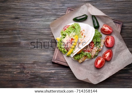 Wooden board with delicious fish tacos on kitchen table