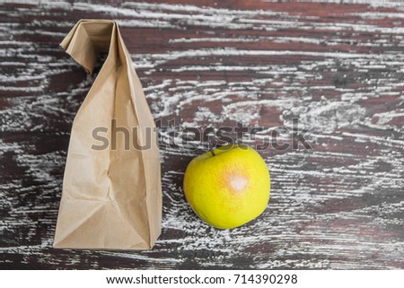 craft paper little bag. brown Paper Bag for food lie on wooden table near with green fresh apple. smiley face. food background