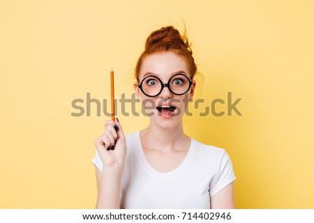 Happy ginger woman in eyeglasses having idea and looking at the camera over yellow background Royalty-Free Stock Photo #714402946